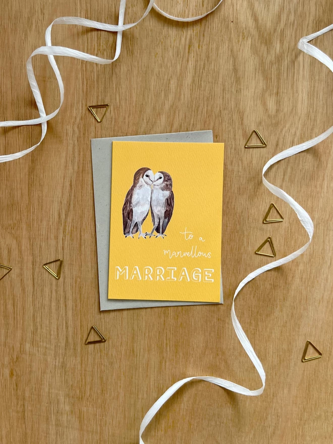 a greetings card with a bright yellow background featuring two kissing barn owls and the phrase ‘to a marvellous MARRIAGE”