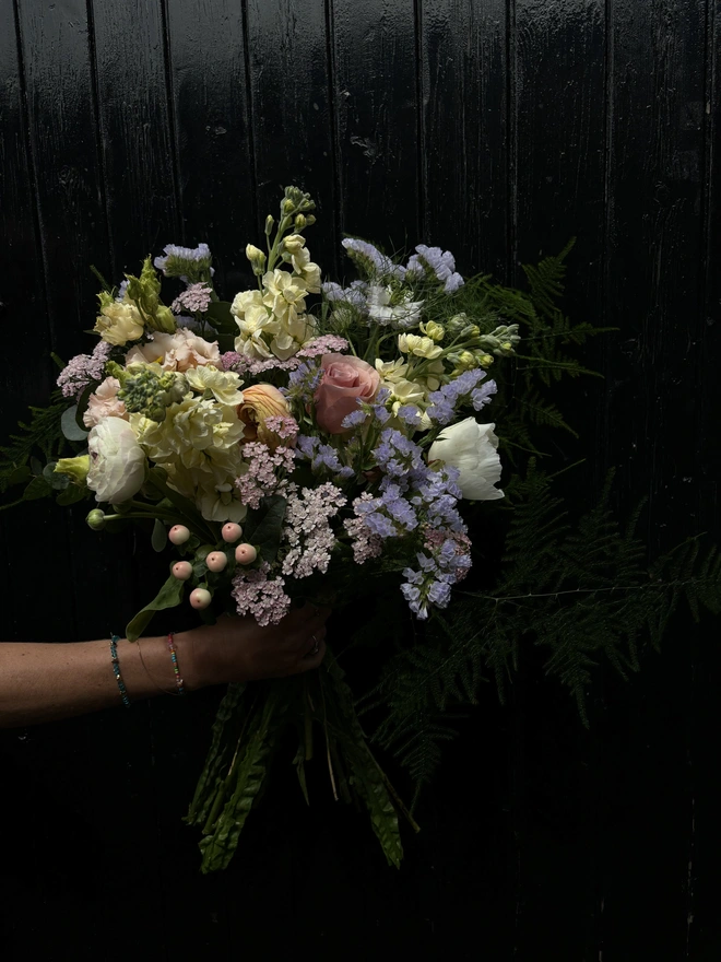 A bouquet of pastel hand tied flowers being held up on a dark background