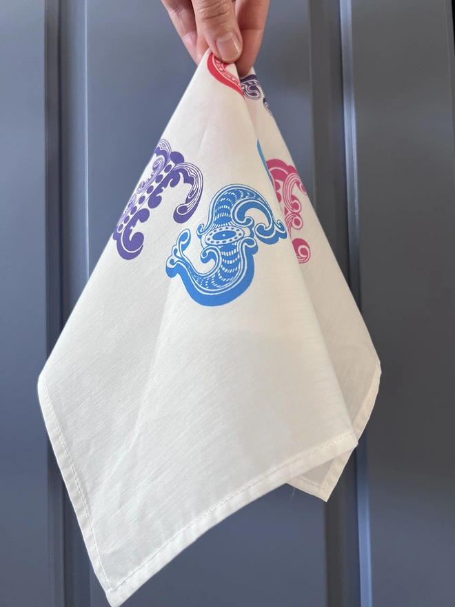 A Mr.PS Love You Lots Multicolour handkerchief held by one hand in front of a blue background