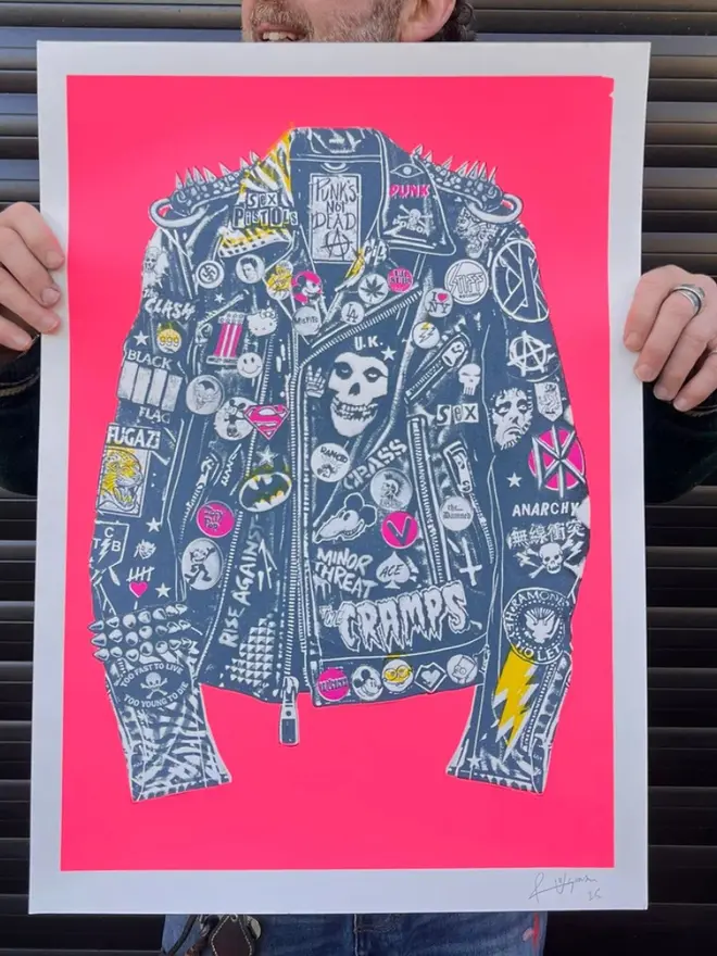 A punk leather jacket decorated with music band patches against a neon pink background.