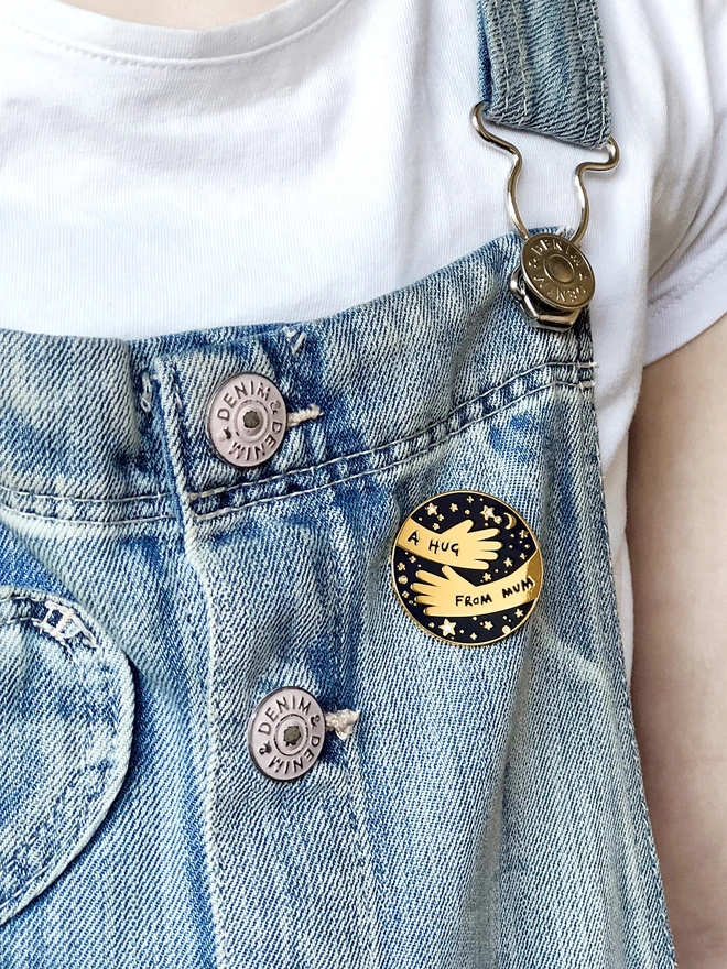 Child wearing dungarees with A Hug From Mum Navy blue and gold pin badge attached.