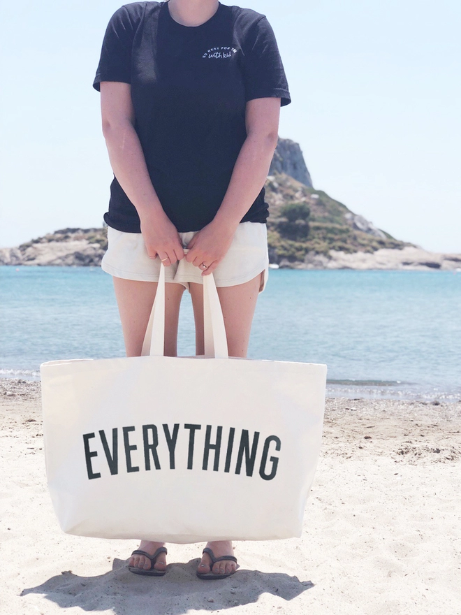Model carrying the Everything oversized tote bag in natural canvas at the beach