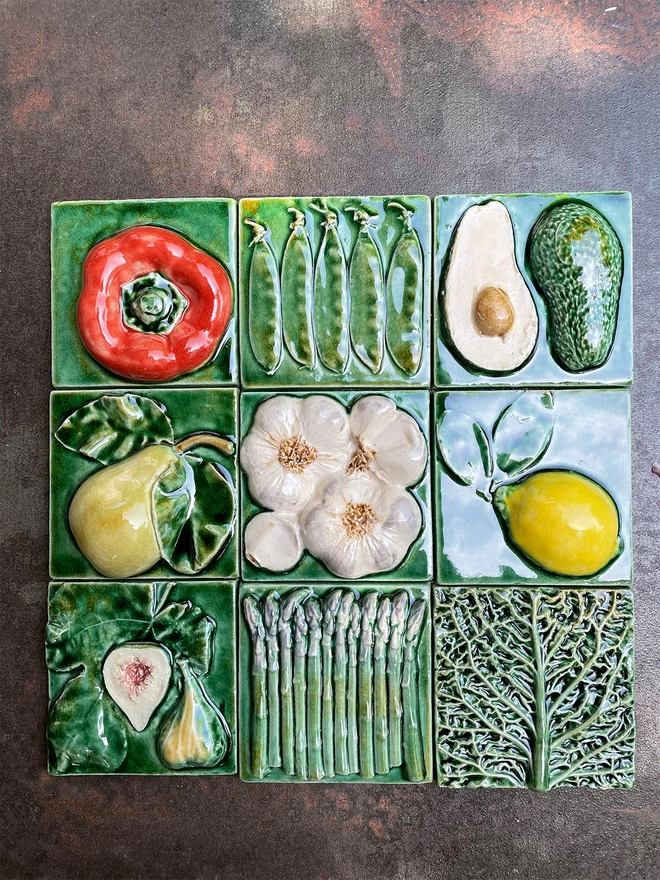 Group of nine different tiles, displayed in a 3x3 grid. Red pepper, mange tout, avocado, pear, garlic, lemon, fig, asparagus, savoy cabbage. Original, unique Fruit and Vegetable tiles, lush green glazes, beautiful textures and colours.  