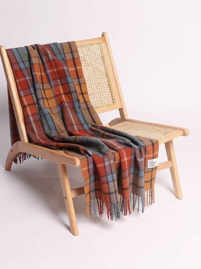 Buchanan Antique Blanket, a colourful blanket draped over a wooden chair on a white surface against a plain backdrop. 