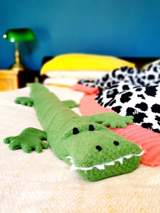 Claude the crocodile lies diagonally on a bed, looking like he is mischievously crawling towards the camera. 