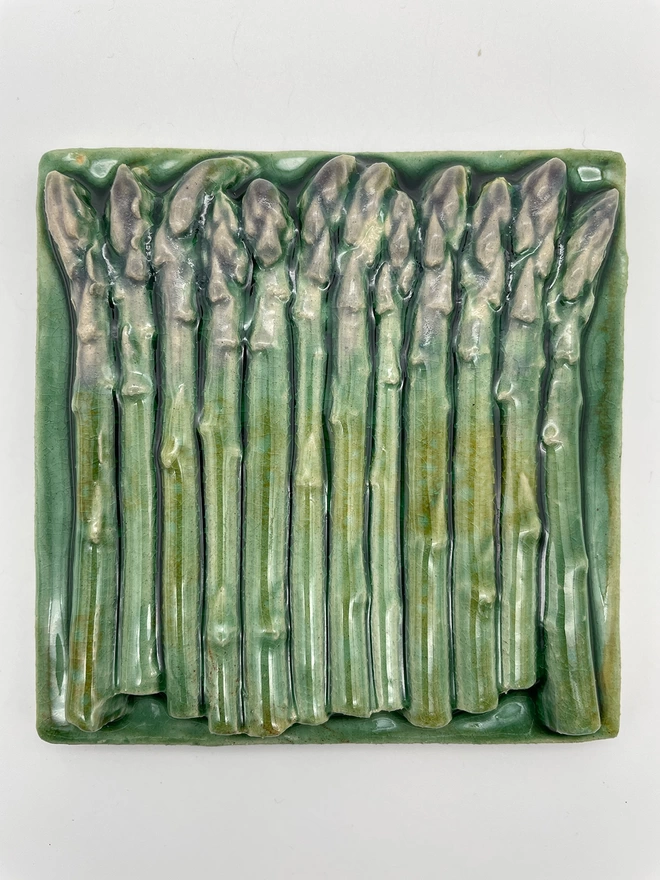 Handmade ceramic tile made from a plaster cast of a bunch of real asparagus spears, side view. Very realistic, three-dimensional, with lush coloured glazes.