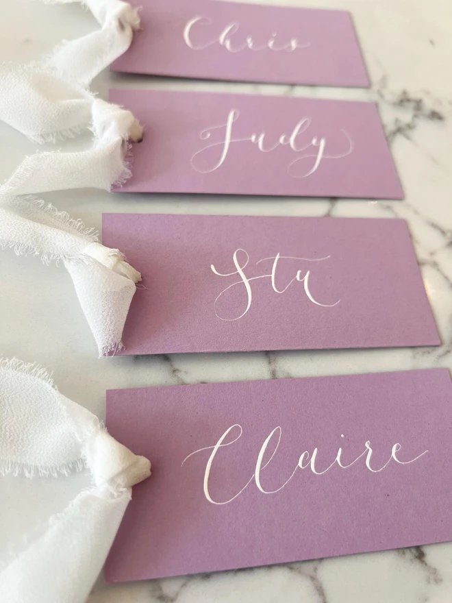 Personalised Calligraphy Wedding Lilac Place Cards, lilac place cards grouped together on a table. 