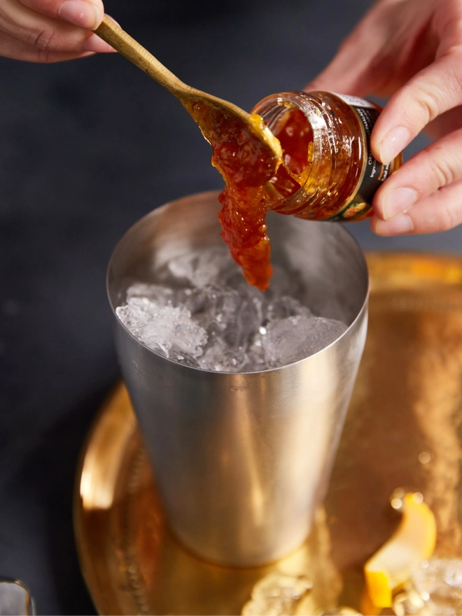 Scooping marmalade into a cocktail shaker filled with ice