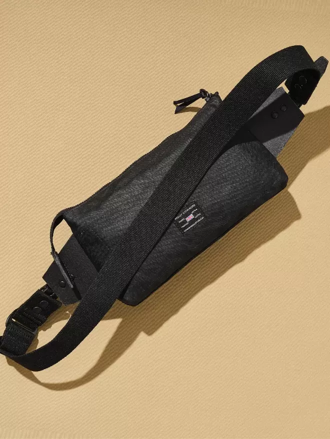 Back view of a black sling bag with black leather trim showing woven label.