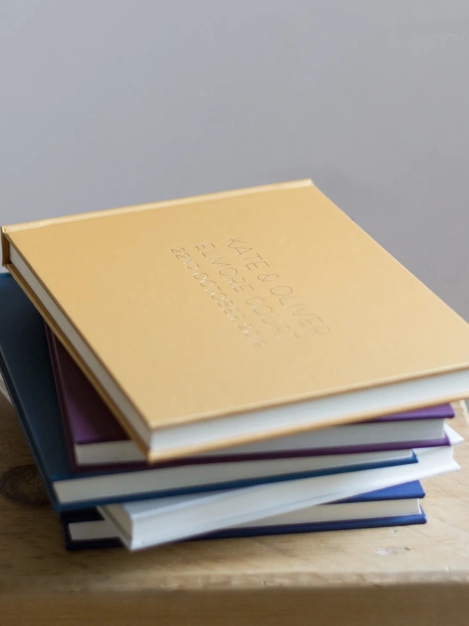 Personalised Luxury Guest Books For A Home, piled upon on a wooden surface. 
