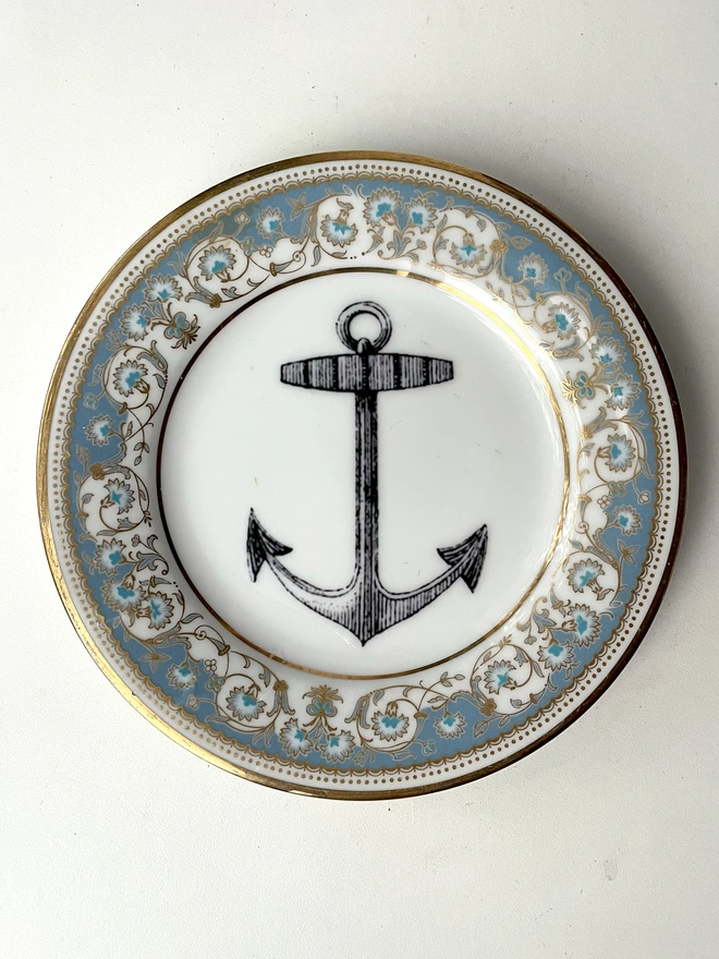 vintage plate with an ornate border, with a printed vintage illustration of an ship's anchor in the middle 