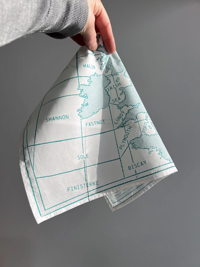 A white hand holds a green printed Shipping Handkerchief against a wall