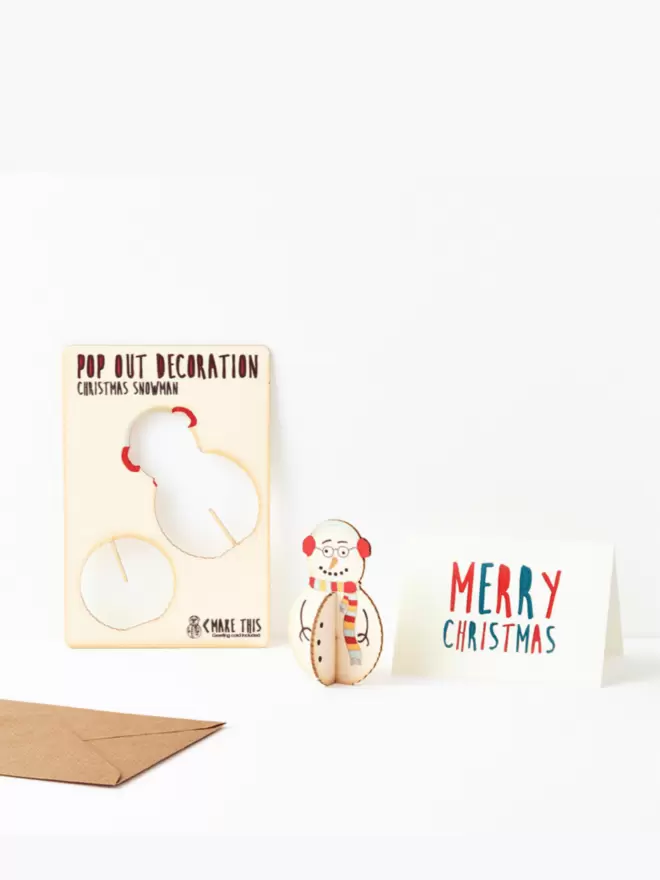 Pop out snowman Christmas decoration and Merry Christmas card and brown kraft envelope on a white background