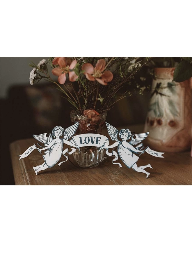 Faith, Love, Hope, wooden banner held by 2 angels, displayed with fresh flowers