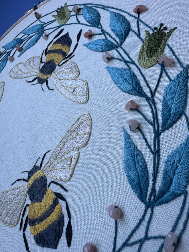 Close up of embroidered bees flowers leaves beads blue green coral 