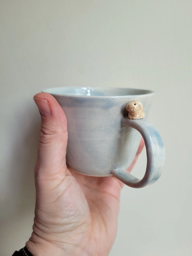Grey pottery bunny cup held in a hand with translucent glaze 