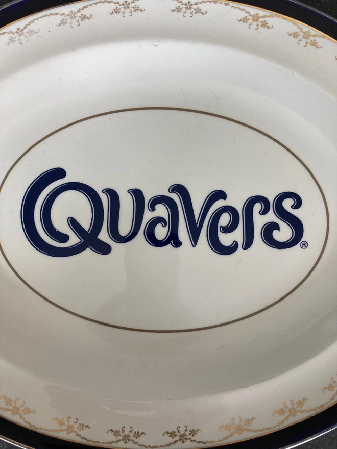 oval vintage china plate with a navy rim, featuring a navy blue 'Quavers' logo across the centre.