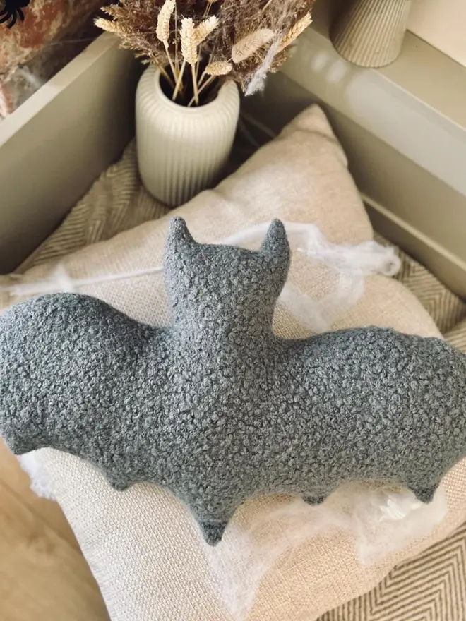 boucle bat pillow. a grey cushion shaped like a bat.