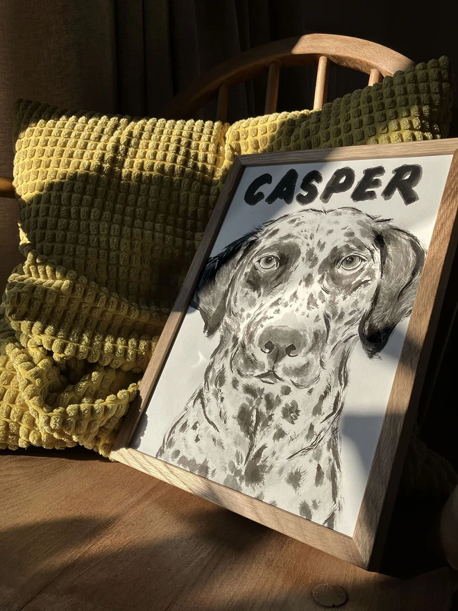 A personalised dog portrait of a Dalmatian by artist 'Dogs by Jeff' in an oak frame sitting on an antique rocking chair in sunset