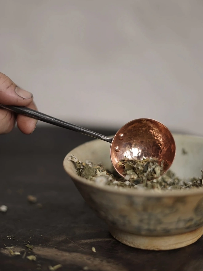 Copper And Stainless Steel Scoop, a metal scoop sitting on a bowl of herbs. 