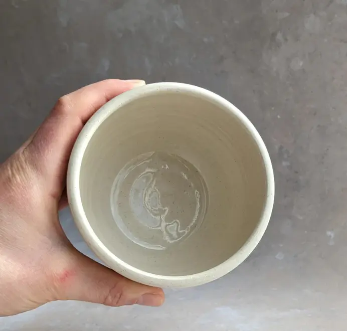 Birds eye view of vanilla bean–colored croissant coffee cup with a subtle croissant design, placed against a grey marble background.