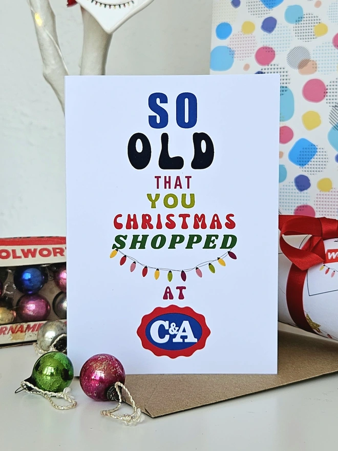 A photograph of the front of a humorous A6 greeting card illustrated using brightly coloured text and the retro shop logo. The text says so old  that you Christmas shopped at C&A with string lights
