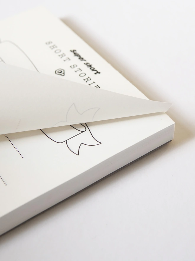 Odd Goose Super Short Stories creative writing notepad close up of page being lifted off