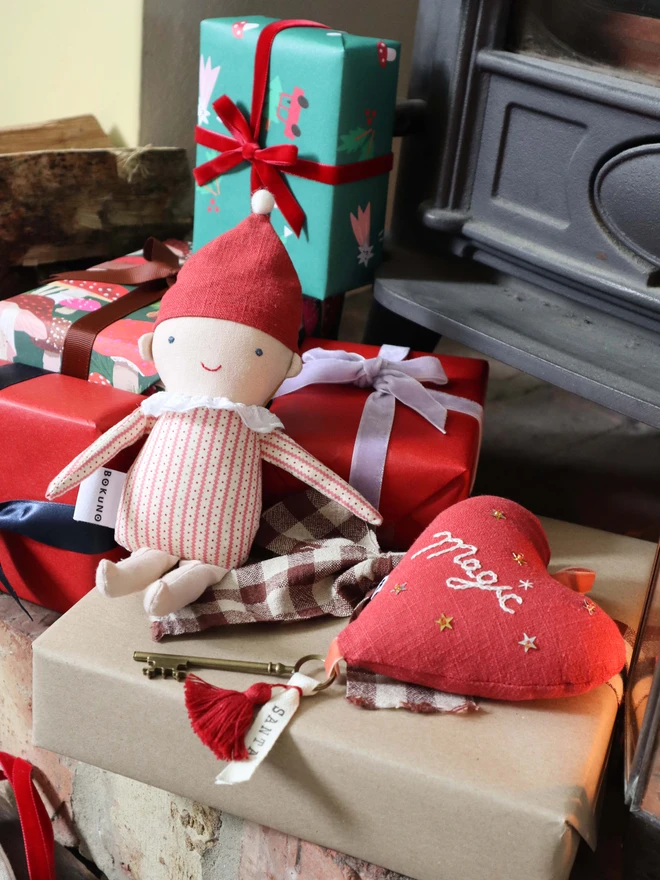 Linen heart ornament with Magic embroidery, hanging rustic key with Santa's name tag and red tassles, surrounded by Christmas presents and elf doll.  