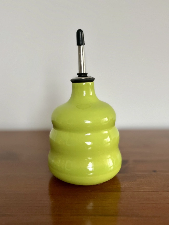 lime green ceramic oil bottle with a chubby form sitting on a dark wood table