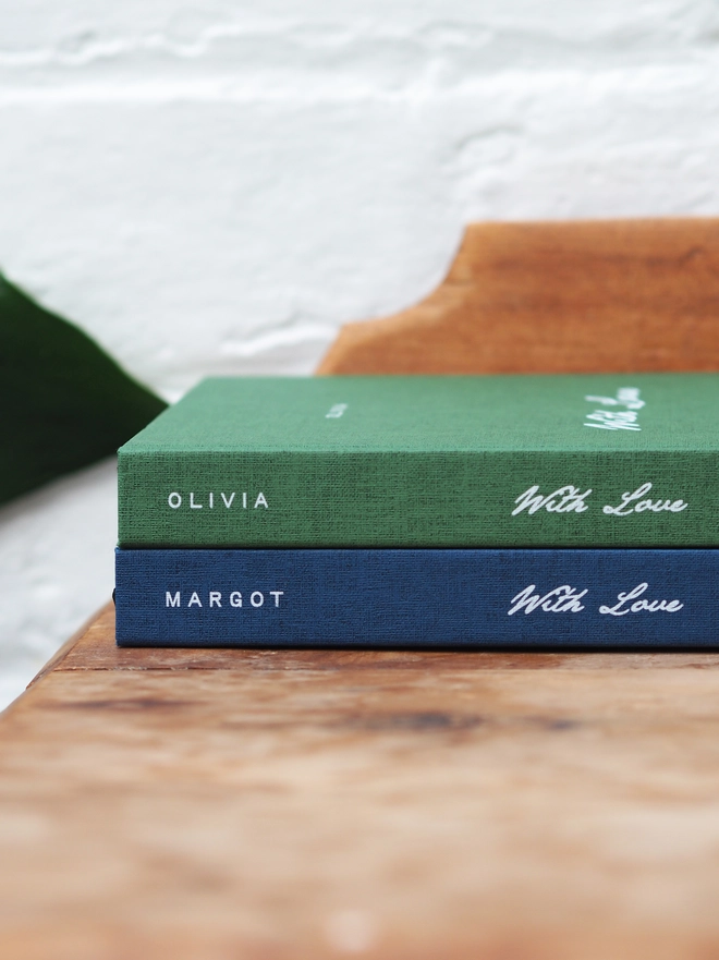 Personalised Hardcover With Love Notebook. A green and a Navy hardcover notebooks with the words With Love in the middle of the spine and personalised with a name at the top.