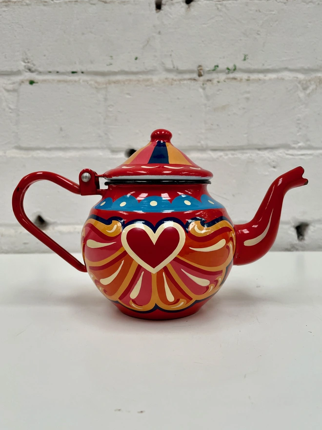 Small red vintage enamel teapot, hand painted with a traditional fairground inspired design in pink, orange and yellow. Teapot has a hinged lid.