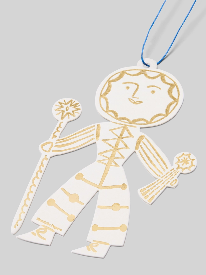 Decorative card cutout of a Sun Folk decoration in gold and white on a gray background.