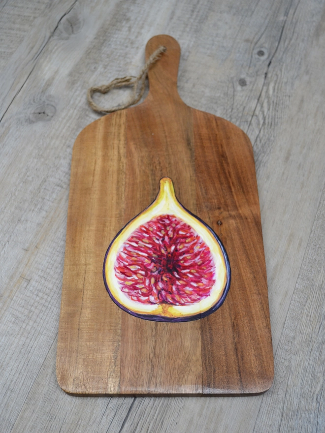 A wooden serving board with a handpainted design of a ripe fig