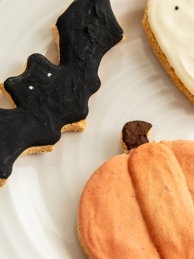 Close-up of pumpkin, ghost and black bat Halloween iced dog biscuits on a cream plate.