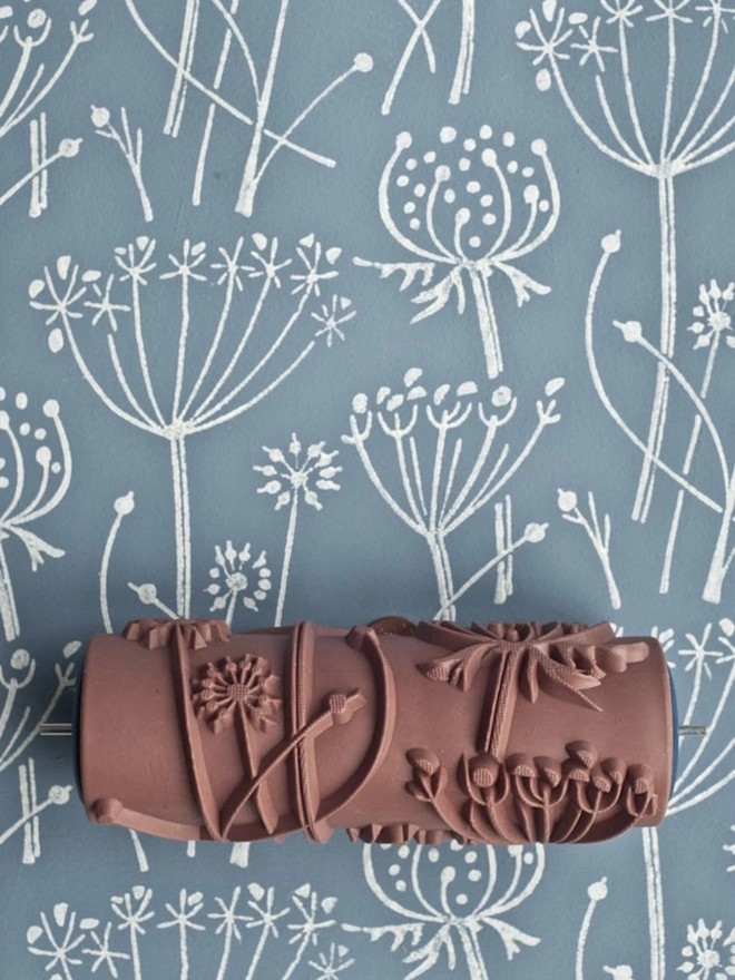 Tussock Patterned Paint Roller, the roller and a blue and white floral pattern on the wall behind. 