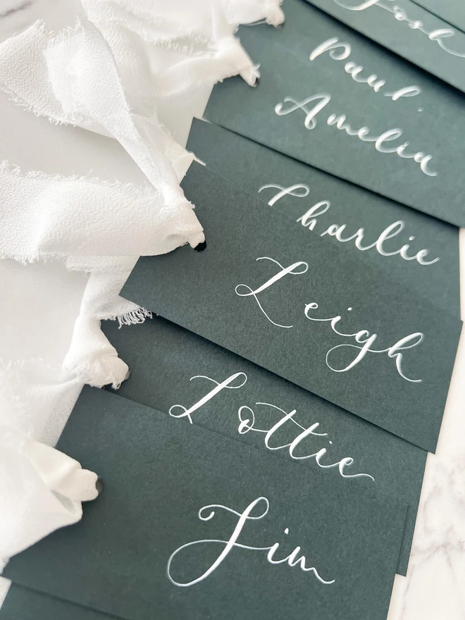 Personalised Calligraphy Wedding Forest Green Place Cards, grouped together with white ribbon. 
