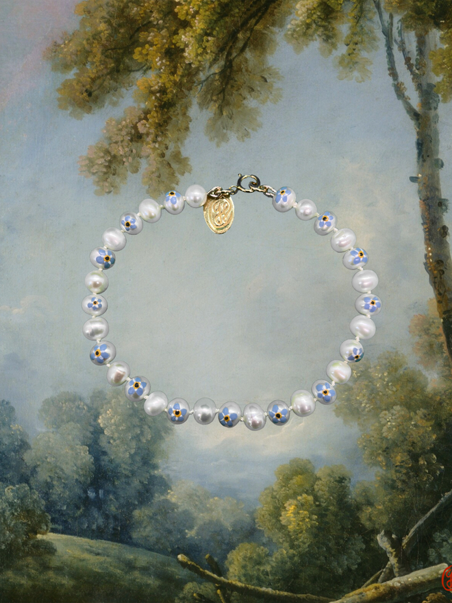 A pearl bracelet with every other pearl painted with a forget me not flower motif, finished with gold findings and a stamped brass tag.