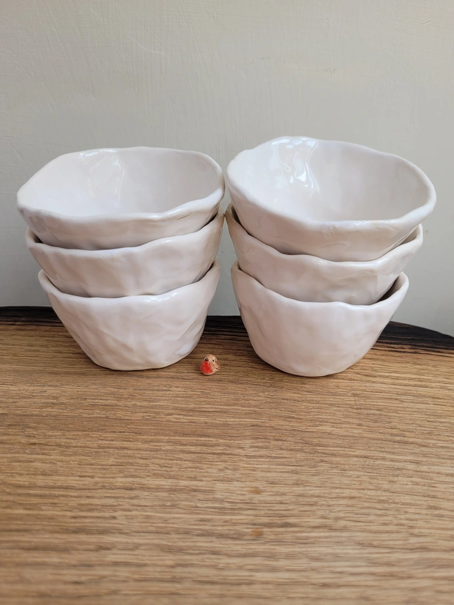 two stacks of white pottery pinch pots with a tiny ceramic robin in between