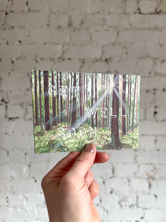 a greetings card featuring an illustration of a woods landscape with the text “get well soon”
