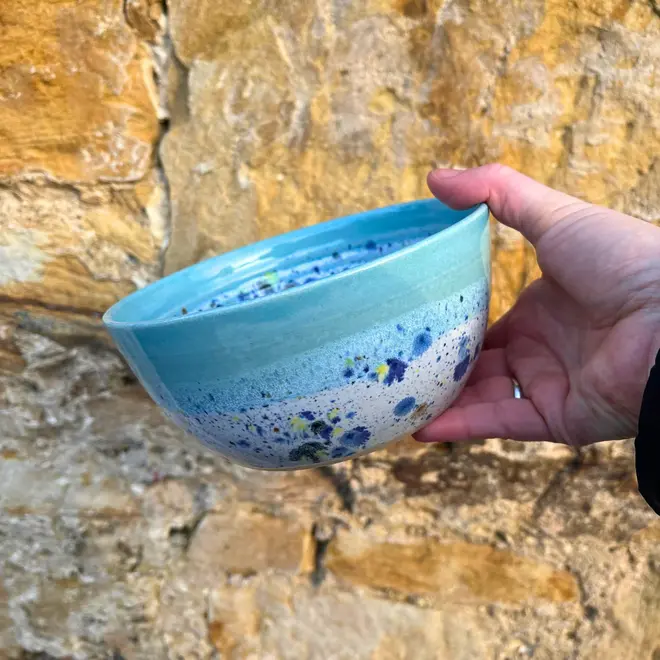 Shoreline Ramen Bowl, a person holding a colourful ramen bowl against a brick backdrop. 