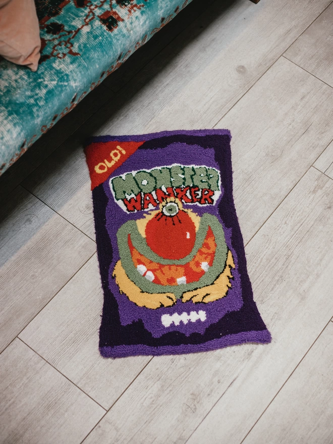 'Monster Wanker' Handmade Tufted Rug/Wall Hanging seen on a wooden floor next to a patterned blue sofa.