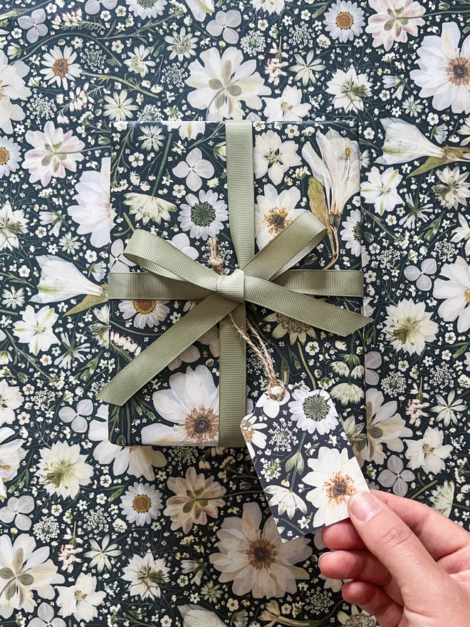 Beautiful wrapping paper and gift tag created from pressed white flowers on a black background.