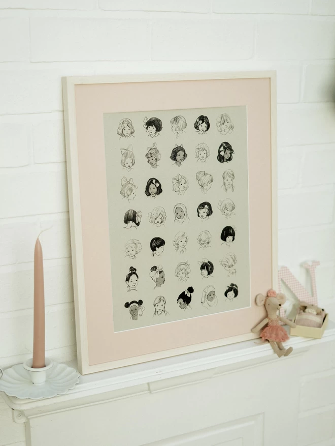 A3 Art print of girls with hairbows printed black on grey card shown in picture frame with pink mount on mantle piece