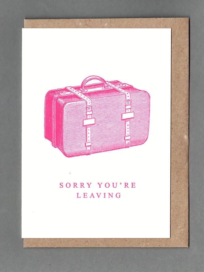White card with pink illustration of a bag with text reading 'Sorry You're Leaving' with a brown envelope behind