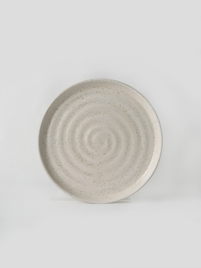 A handmade ceramic cake plate in pepper white glaze, photographed from the front against a plain light grey background, showing a natural concentric swirl texture and a shallow raised rim