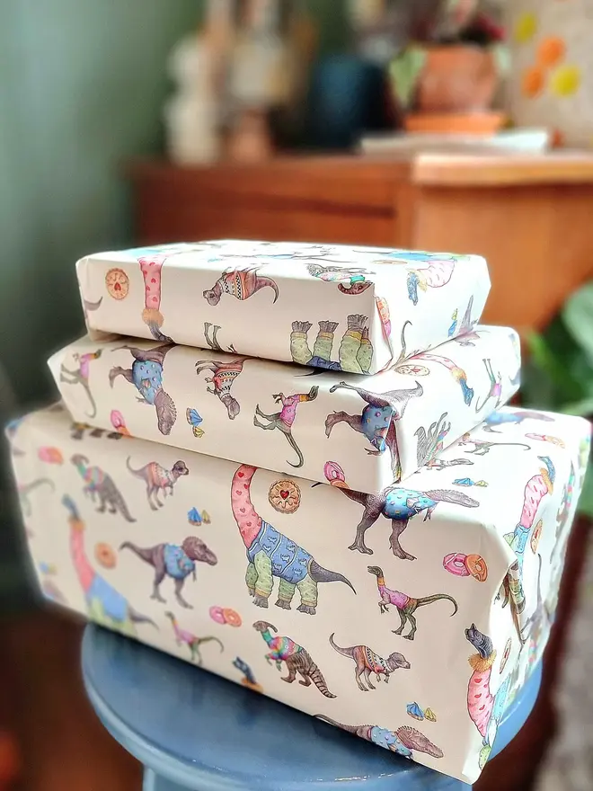 illustrated dinosaurs and biscuits wrapping paper sheets. 3 boxes each wrapped a sheet of cream wrapping paper featuring illustrated dinosaurs and biscuits.