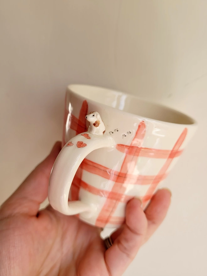 a red gingham cup held in a hand with a tiny brown and white puppy dog and red hearts on the handle
