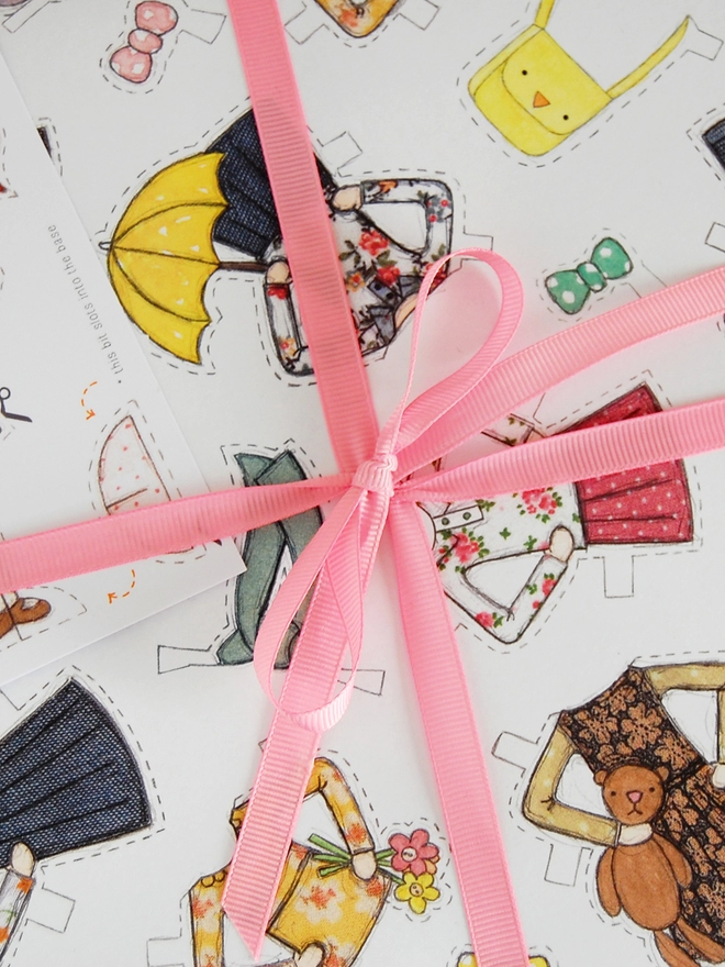 A gift wrapped in wrapping paper with illustrated outfits for the included paper doll tag.