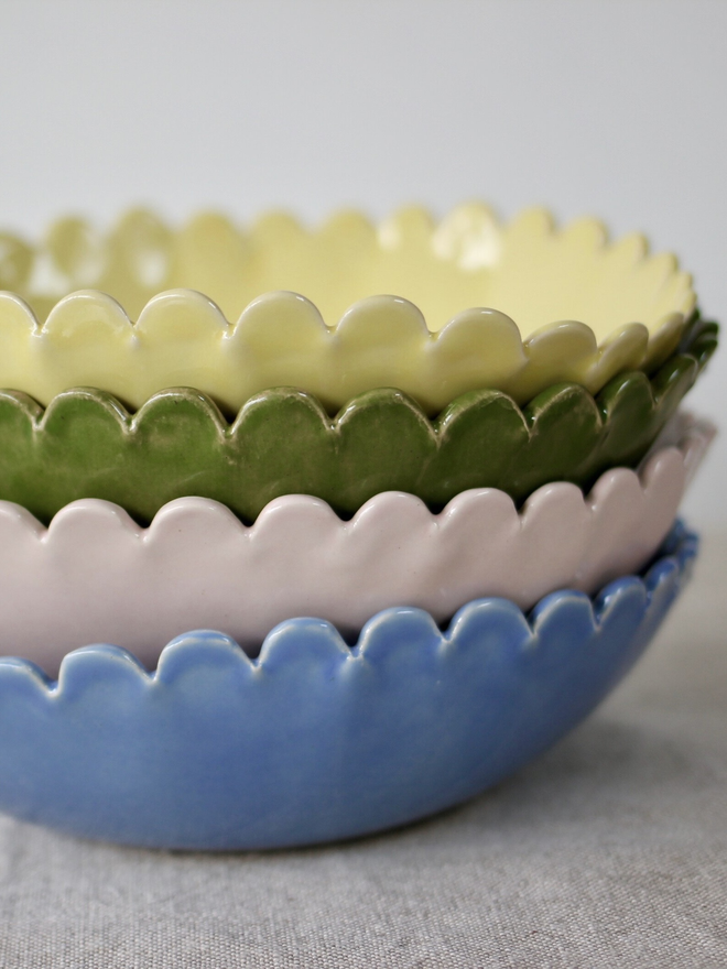stack of four daisy edge small serving bowl, periwinkle blue, blossom pink, olive green, butter yellow