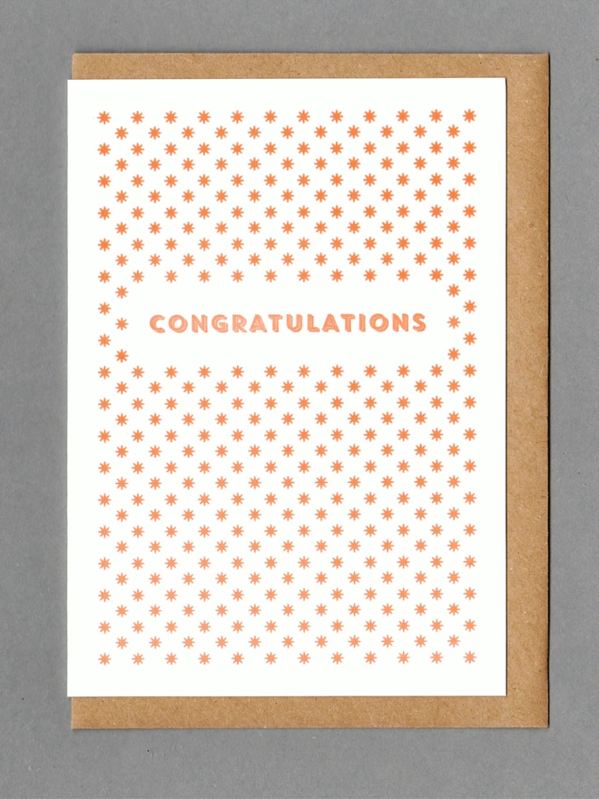 White card with orange stars and orange text reading 'CONGRATULATIONS' with a kraft envelope behind it